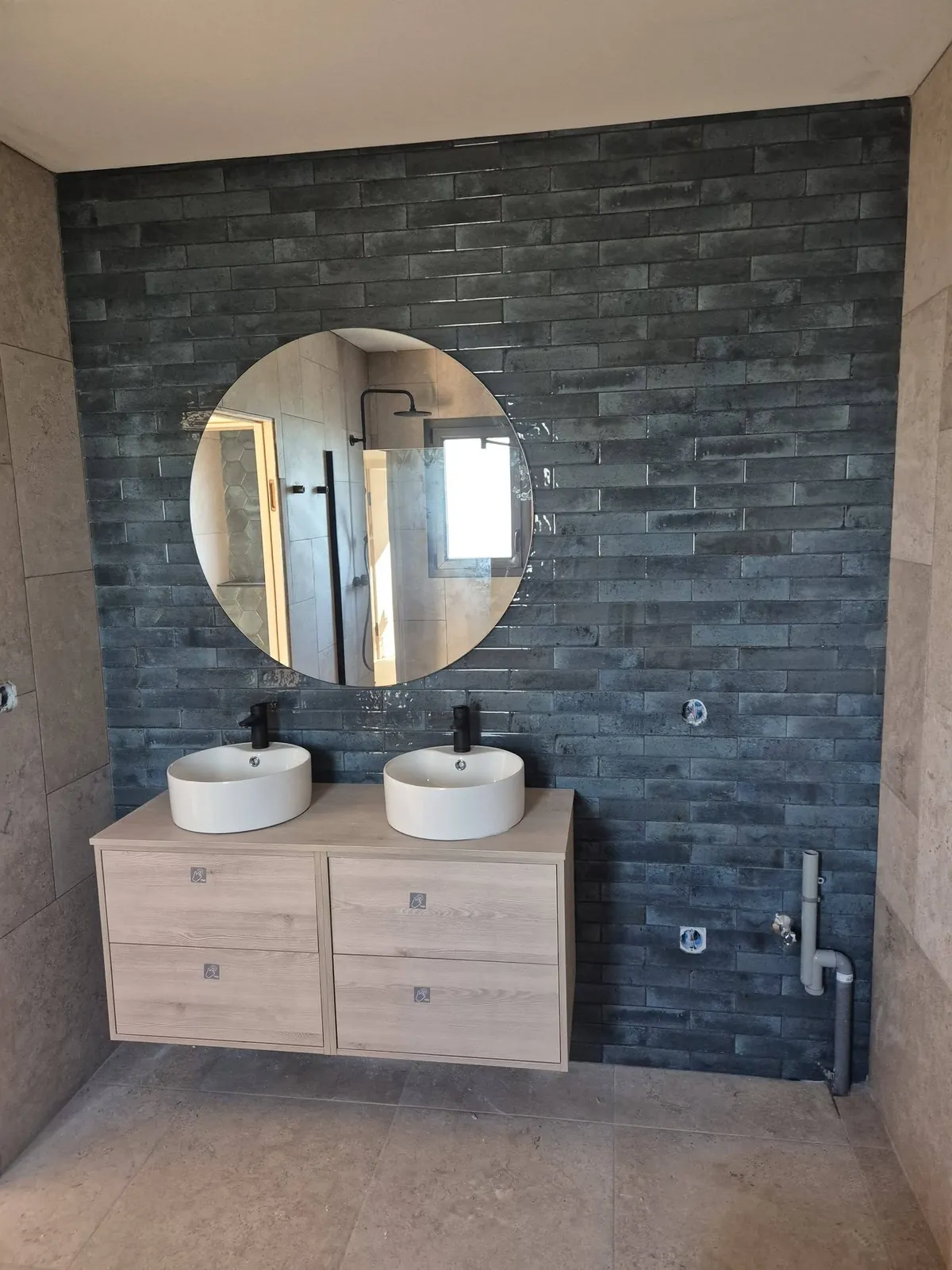 Salle de bain rénovée : double vasque sur meuble bois clair, miroir rond et zellige vert foncé
