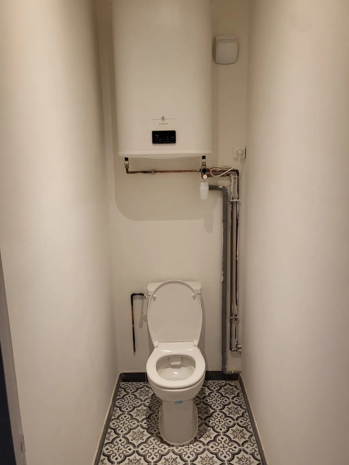 Après : WC refaits avec carreaux de ciment au sol et chauffe-eau neuf fixé au mur