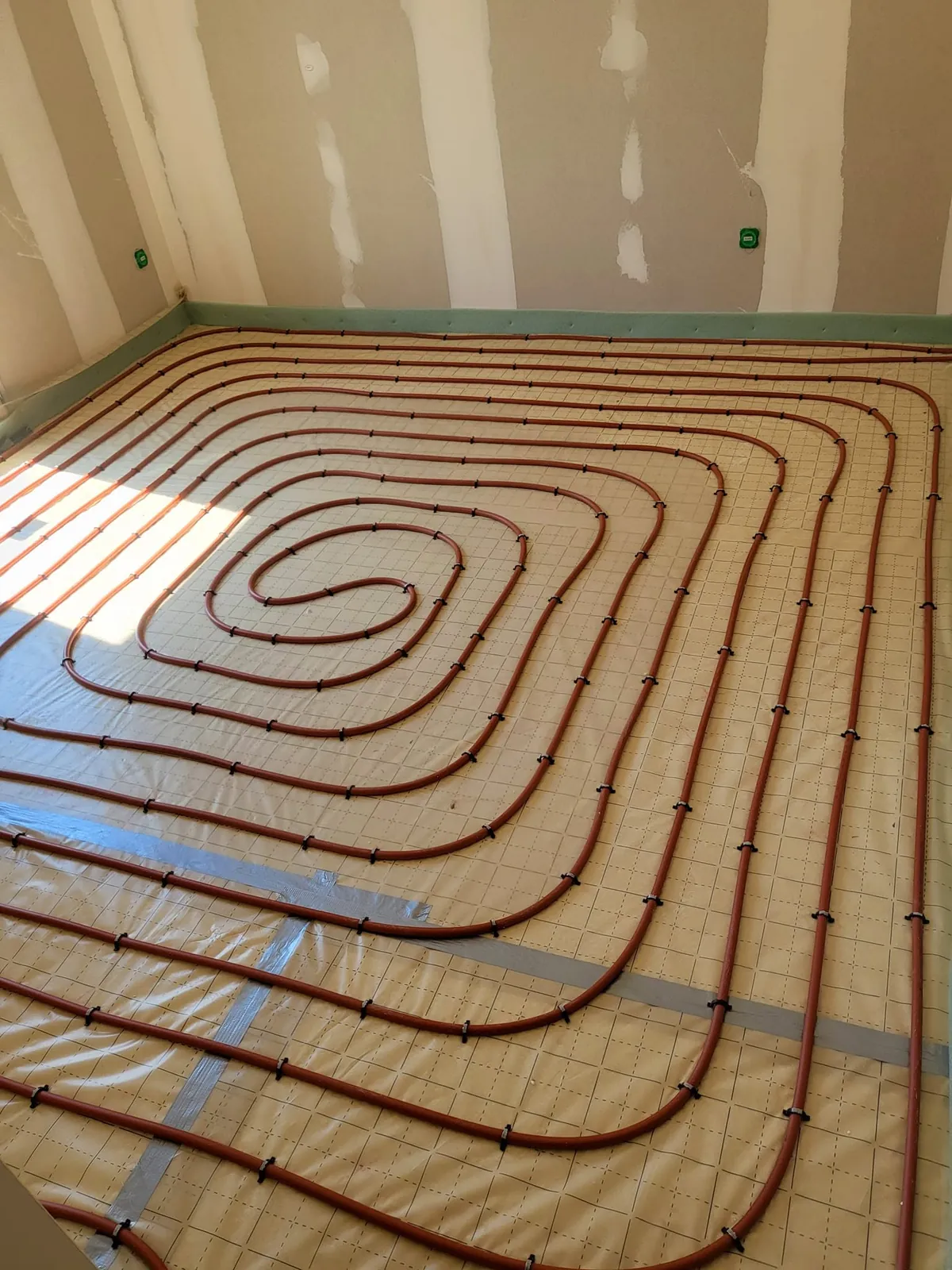 Plancher chauffant posé en boucles serrées dans une pièce de maison neuve, avant la chape